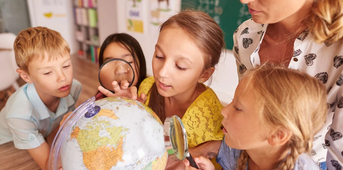 Children and teacher examining a globe in a classroom setting